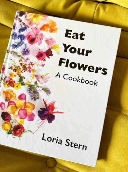 Lori stern's cookbook called "eat your flowers" about cooking and baking with flowers sits on a yellow cushion.