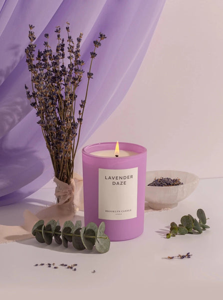 a frosted purple glass candle in the scent lavender daze by Brooklyn candle company sits next to pieces of eucalyptus and lavender