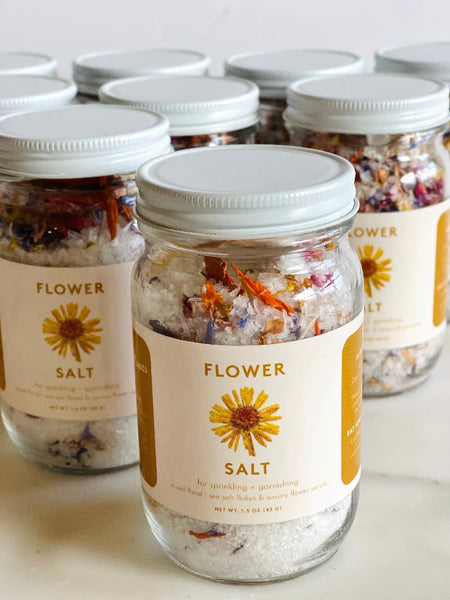 multiple jars of Loria stern's Eat Your Flowers organic edible Flower Salt garnish sit in rows on a marble table.
