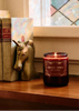 Candle with decorative packaging on a shelf next to books and a horse head bookend.