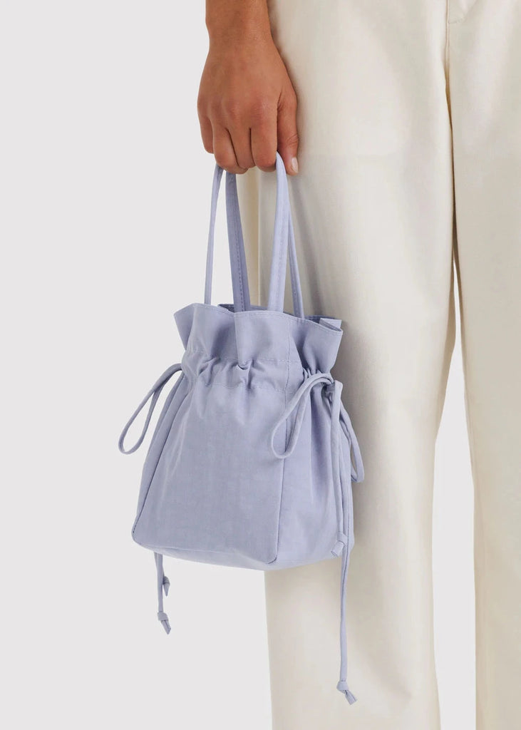 Light blue drawstring bag held by a person wearing light-colored pants on a white background