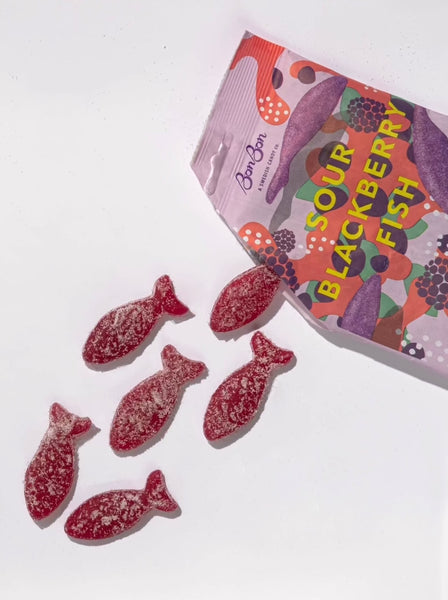 sour blackberry gummy fish spilling out of an opened illustrated bonbon nyc candy bag on a white background
