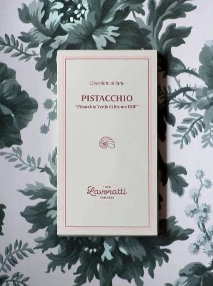 A box of Cioccolato Lavoratti 1938 Milk Chocolate Pistachio Cream bar sits in front of a floral background. 