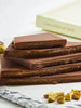 A stack of Cioccolato Lavoratti Pistachio Cream Milk Chocolate Bars sit on a stone slab. The chocolate is broken in half exposing the pistachio cream filled center.