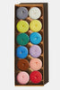 A box set of Rainbow Tea Light Candles sit inside a brown box in neat rows.