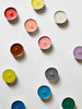 various colorful tea lights from le feu de l'eau sit playfully spread out on a white background.