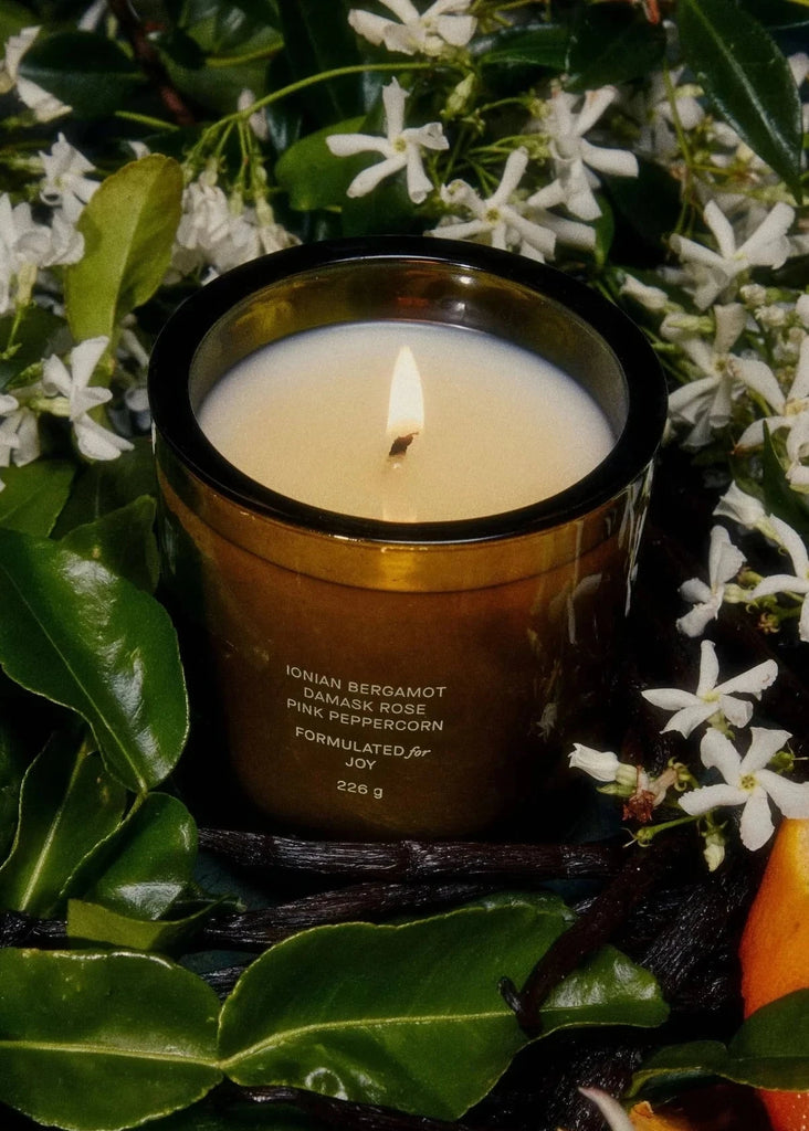 Candle in a decorative container with jasmine flowers and leaves in the background