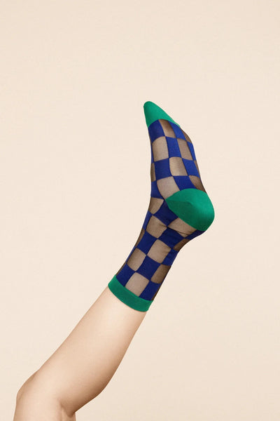 a foot raised in the air wearing Hansel from Basel's jolly checkered sheer crew in navy and green.