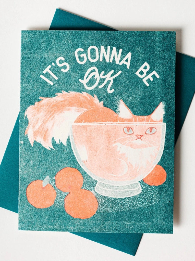 card with illustration of orange cat inside clear bowl with oranges on the table and it's gonna be ok printed above