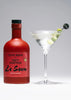 Red bottle labeled 'Olive Brine for Dirty Martinis La Saum' next to a cocktail glass with a drink.