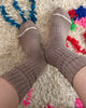 We see two feet wearing a pair of Le Bon Shoppe Ballet Socks in the color Mocha Mousse on a shaggy beige carpet with colorful patterning 