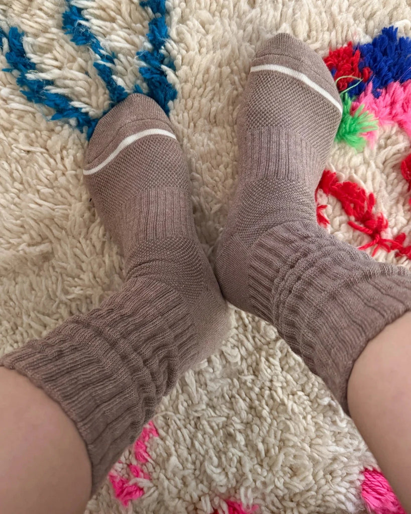 We see two feet wearing a pair of Le Bon Shoppe Ballet Socks in the color Mocha Mousse on a shaggy beige carpet with colorful patterning 