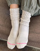 Person wearing a pair of Le Bon Shoppe ballet socks in the color Oatmeal sitting on a brown couch.