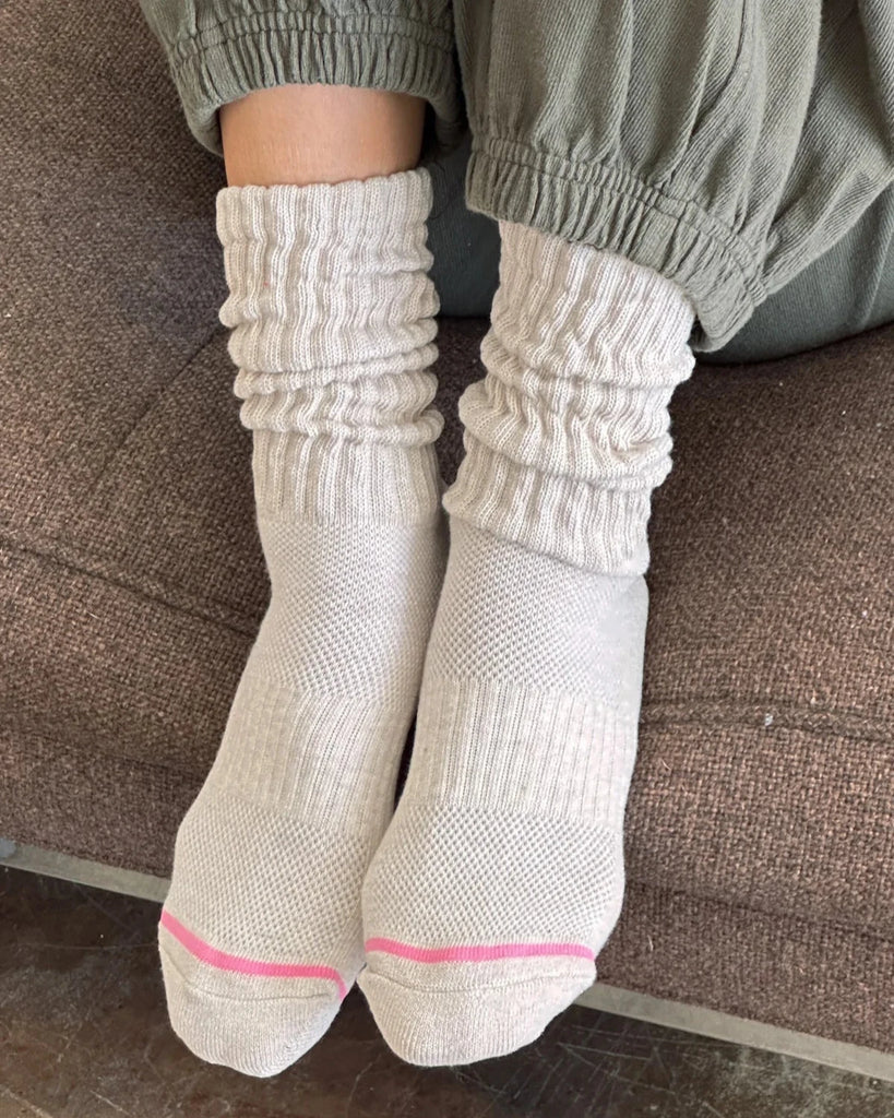 Person wearing a pair of Le Bon Shoppe ballet socks in the color Oatmeal sitting on a brown couch.