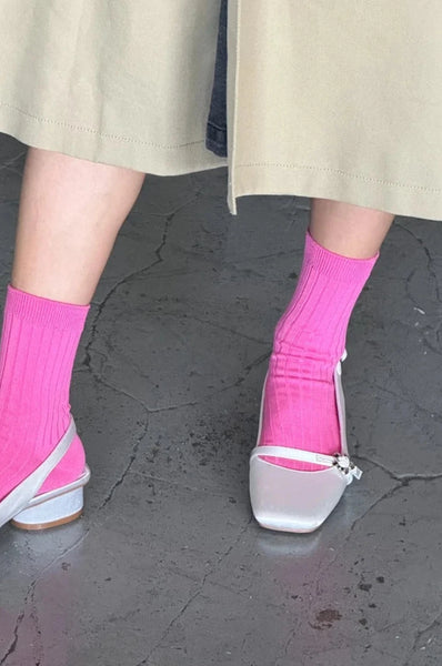 We see the legs of a woman. She is wearing wide leg linen pants, Her mercerized cotton socks in the color bright pink from Le Bon Shoppe with silver strappy slip on shoe