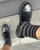A person wearing a pair of Le Bon Shoppe Wally Socks in the color charcoal wide stripe paired with shiny loafers