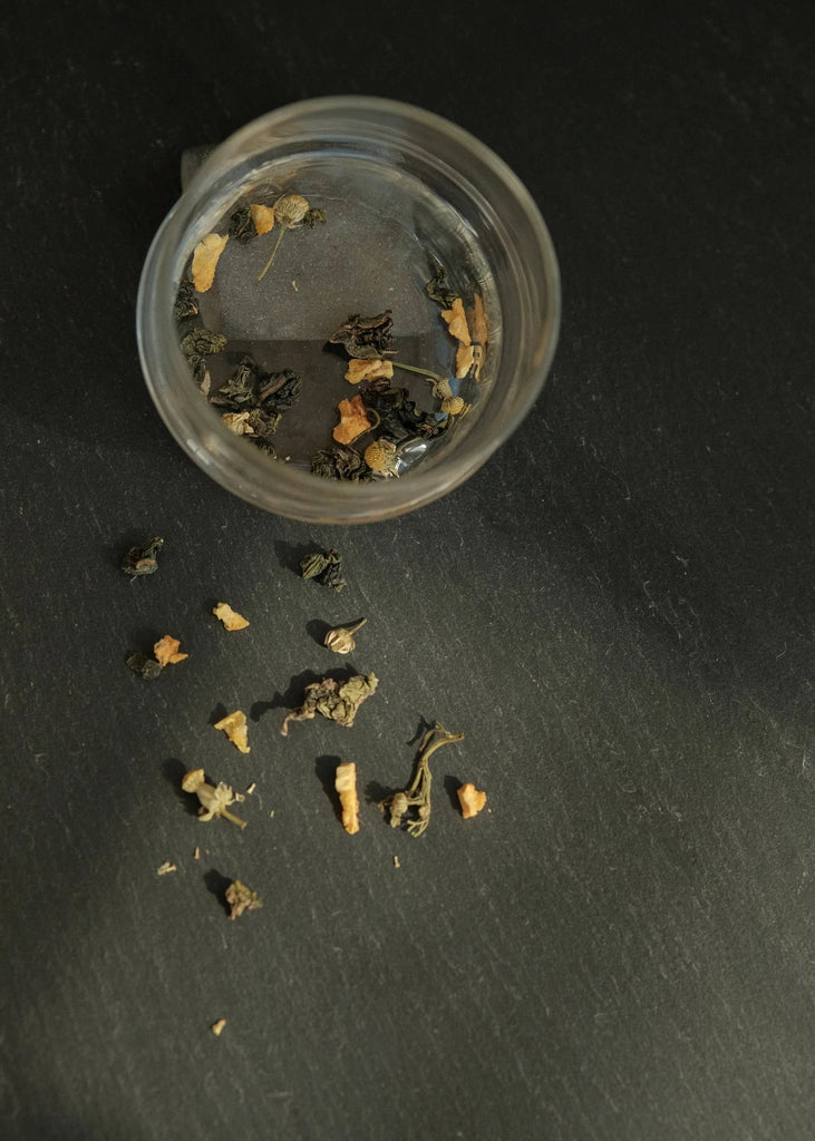 Small container with dried tea on a dark surface