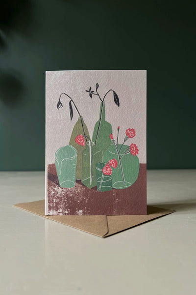 A greeting card featuring an illustration of green bottles and jars with pink carnation flowers from Luiza Holub.