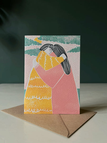 A Luiza Holub greeting card showing two people hugging. Above them clouds are parting and the sun is peeking through.