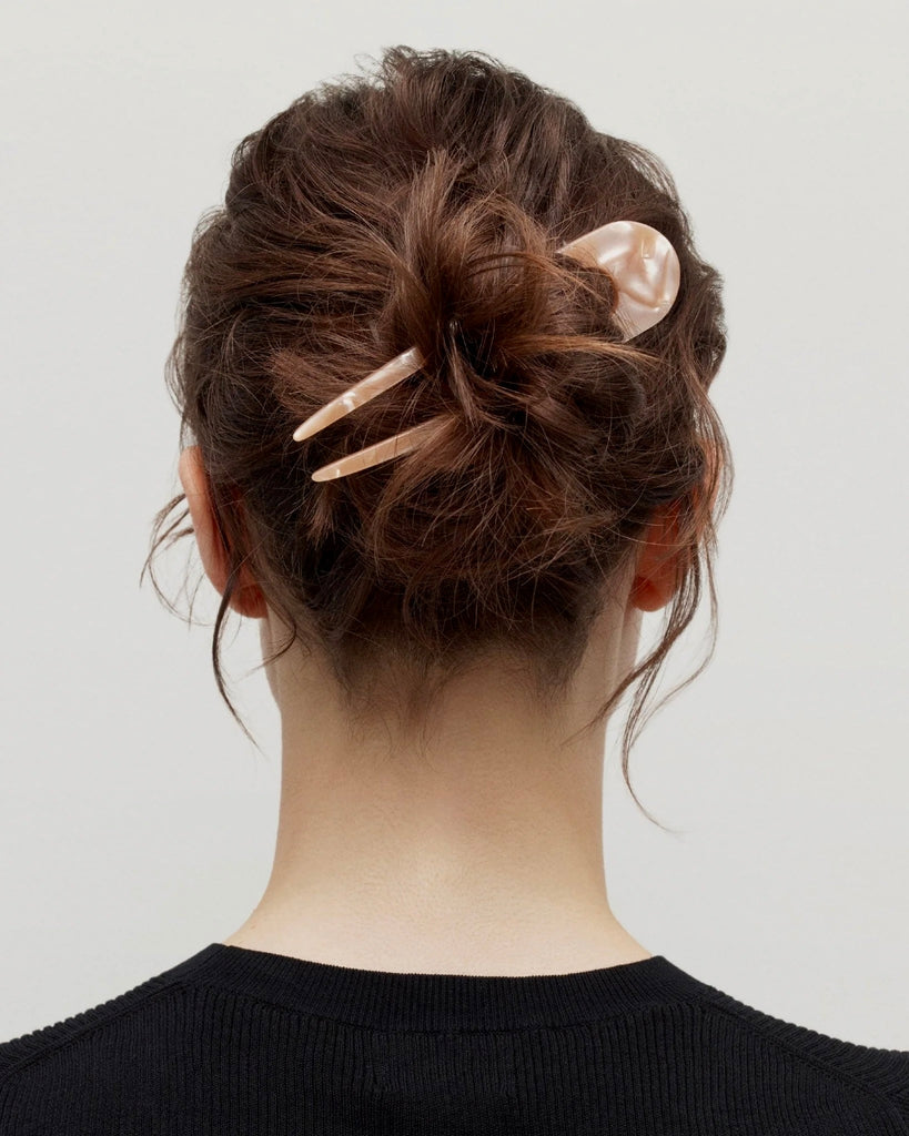 a woman in a black shirt with brown hair wearing a French hair pin by machete.