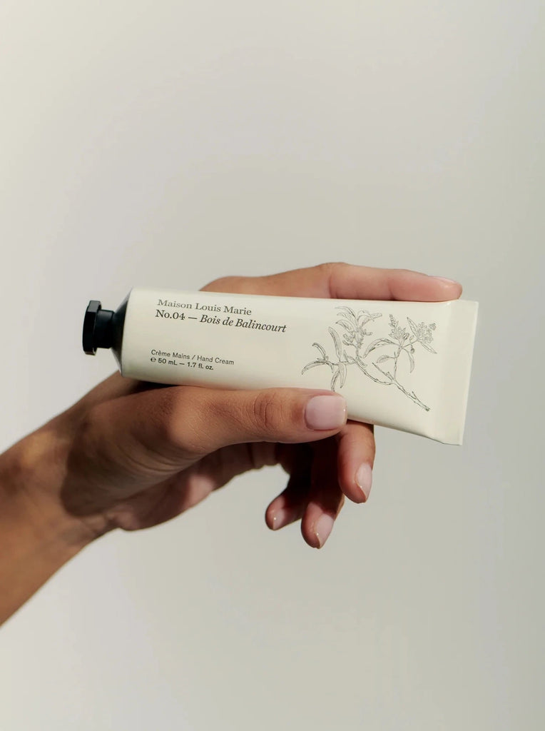 a hand holding a tube of maison Louis Marie's bois de balincourt hand cream in front of a white background.