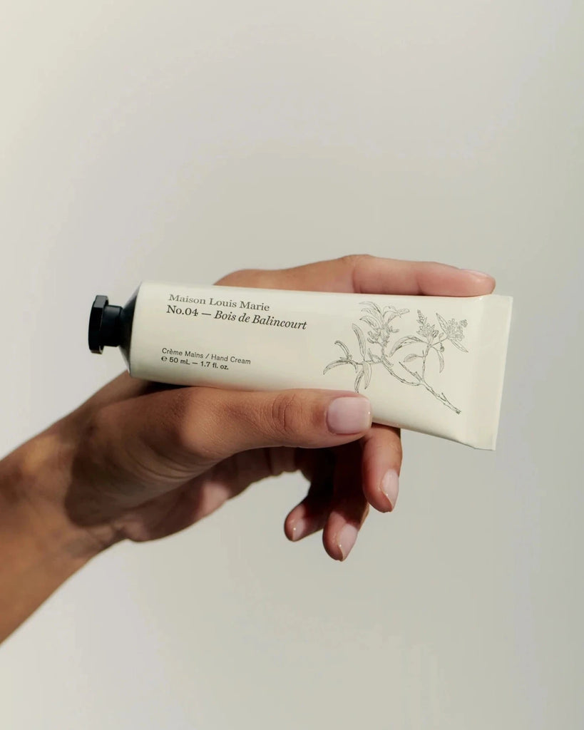 a hand holding a tube of maison Louis Marie's bois de balincourt hand cream in front of a white background.