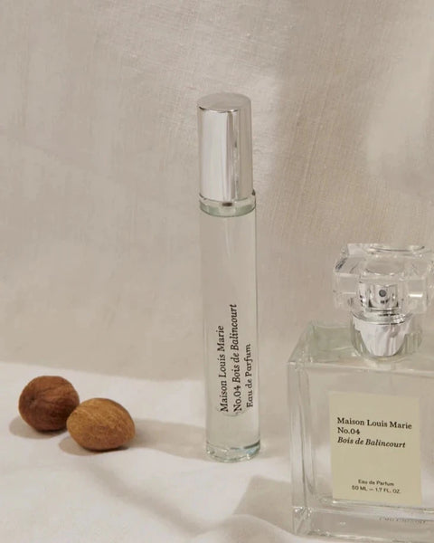 a small glass spray bottle of maison Louis Marie's bois de balincourt edp sits on a cream background next to a full sized bottle of the same perfume and a couple whole nutmeg.