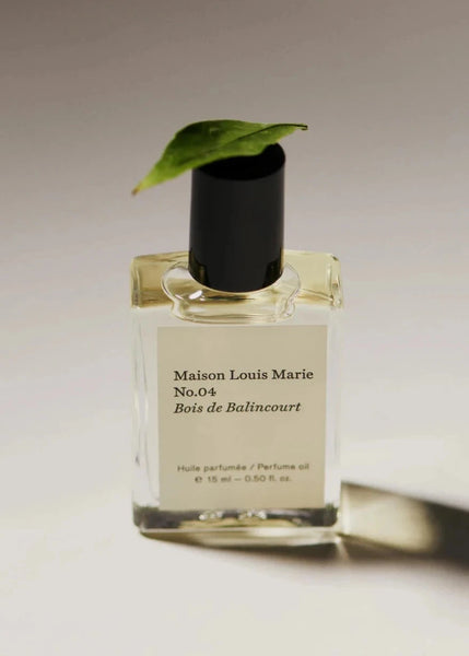 a bottle of maison louie Marie's no. 4 bois de balincourt perfume oil sits on a white background with a leaf resting on the lid.