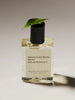 a bottle of maison louie Marie's no. 4 bois de balincourt perfume oil sits on a white background with a leaf resting on the lid.