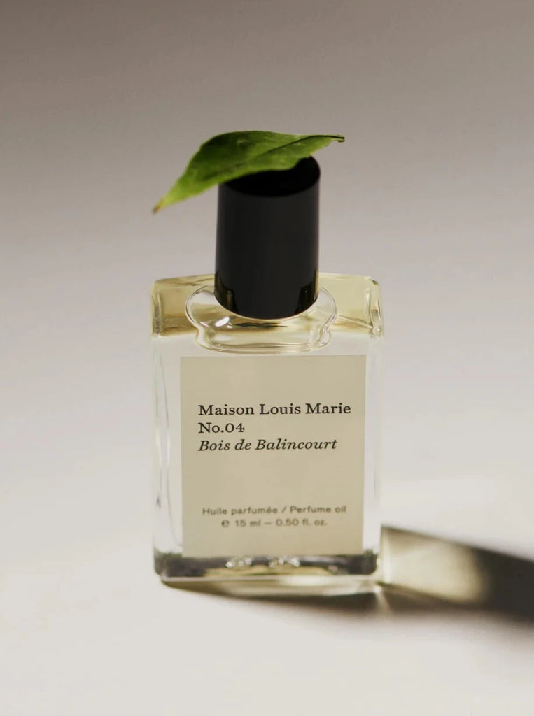 a bottle of maison louie Marie's no. 4 bois de balincourt perfume oil sits on a white background with a leaf resting on the lid.