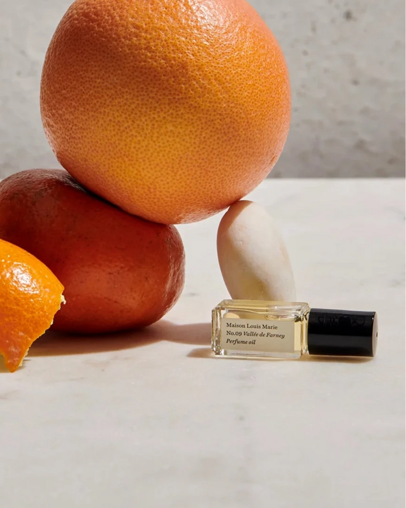 a mini bottle of maison Louis Marie's Valle de farney perfume sitting next to whole oranges on a white table.