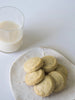 a pile of makabi and sons vanilla earl grey shortbread cookies on a white ceramic plate next to a cup of milk