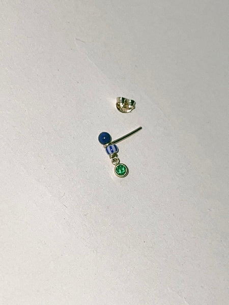 earring with a blue bead, a striped bead, and a green gem sitting beside an earring back against a white background