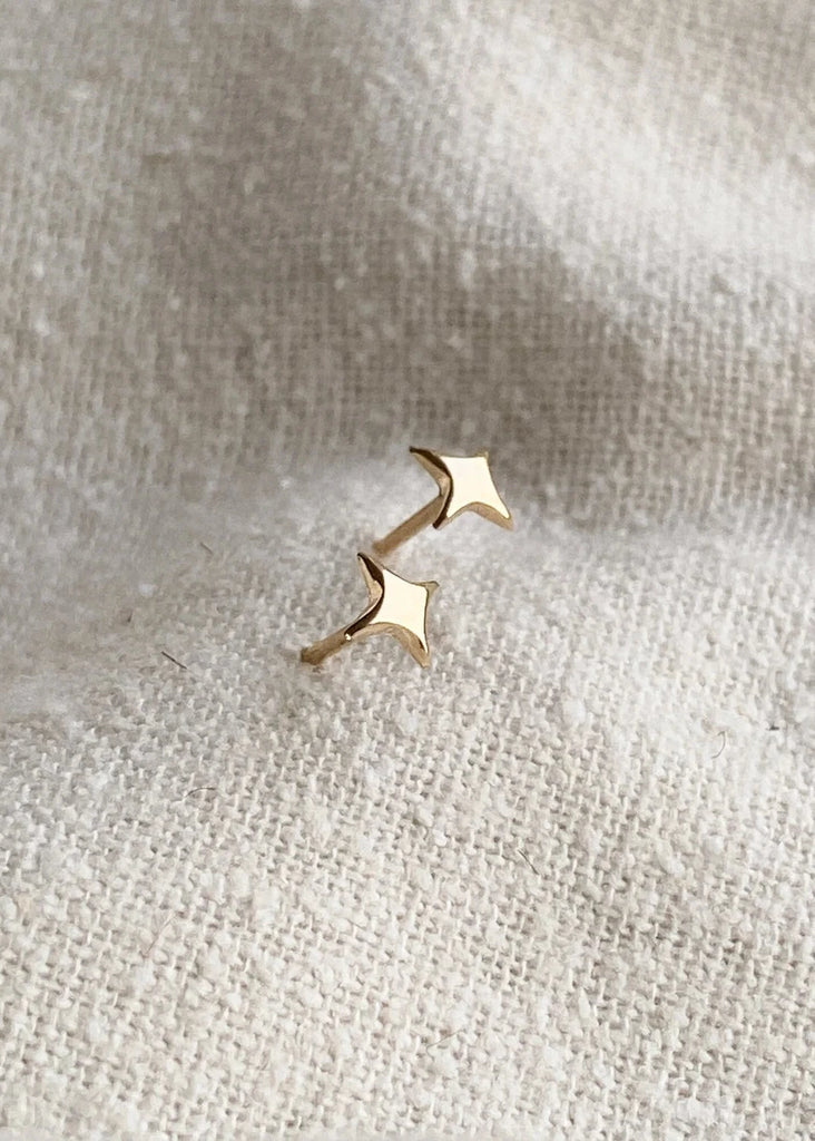 Gold star-shaped earrings on a textured beige fabric background