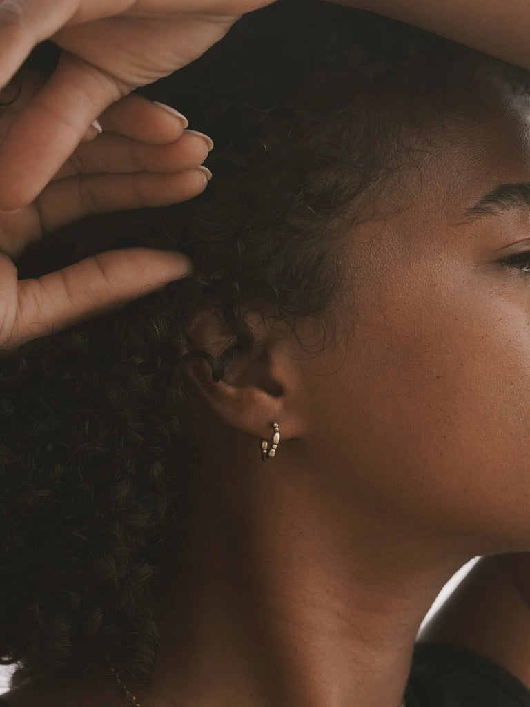 a woman wearing a pair of small brass hoop earrings that look like turned wood - made by Natalie joy jewelry