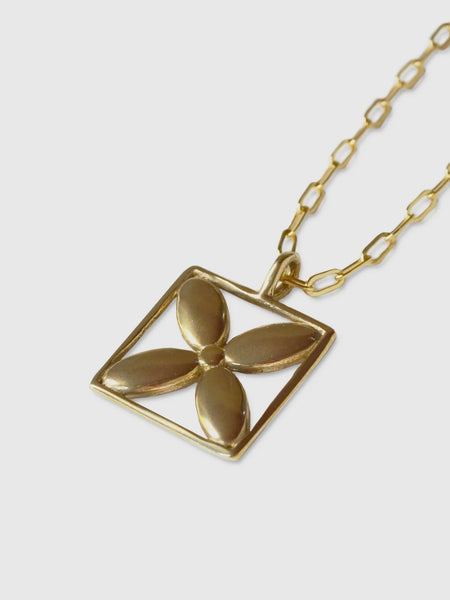 detail of a necklace made by Natalie joy jewelry in brass that looks like a flower inside a square