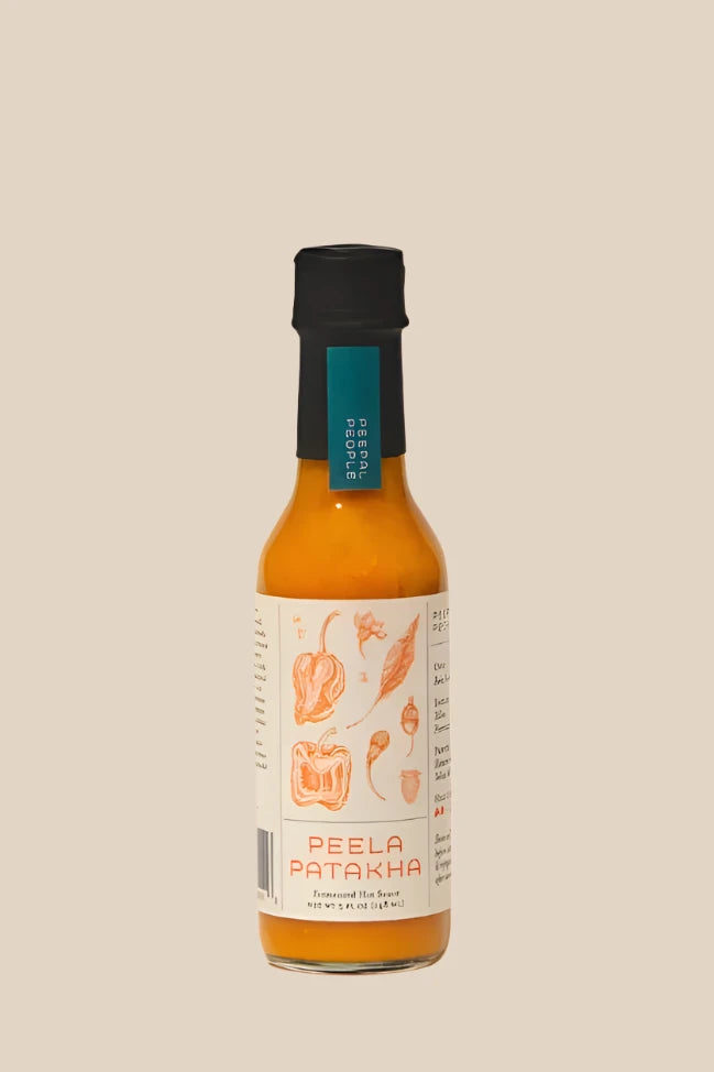 a bottle of peepal people's peela patakha yellow firecracker hot sauce on a creamy beige background