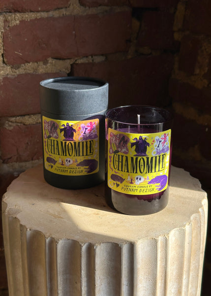 Chamomile candle with packaging on a stone surface against a brick wall.