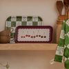 a birchwood tray with illustrated cherries sitting on a shelf with cups and kitchen utensils.