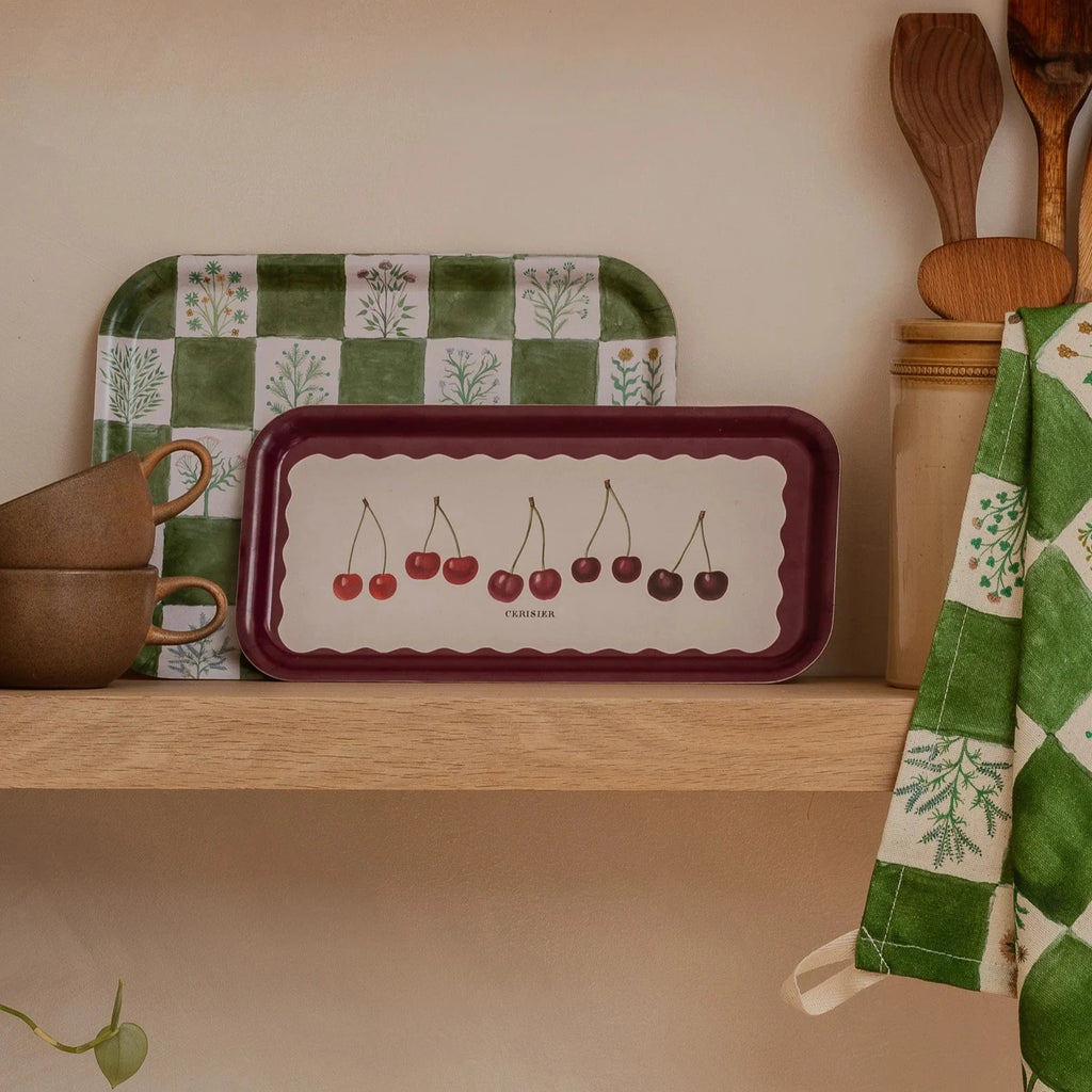 a birchwood tray with illustrated cherries sitting on a shelf with cups and kitchen utensils.