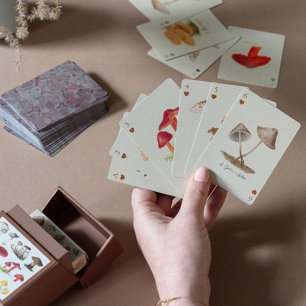 a hand holding a set of playing cards with illustrations of mushrooms.