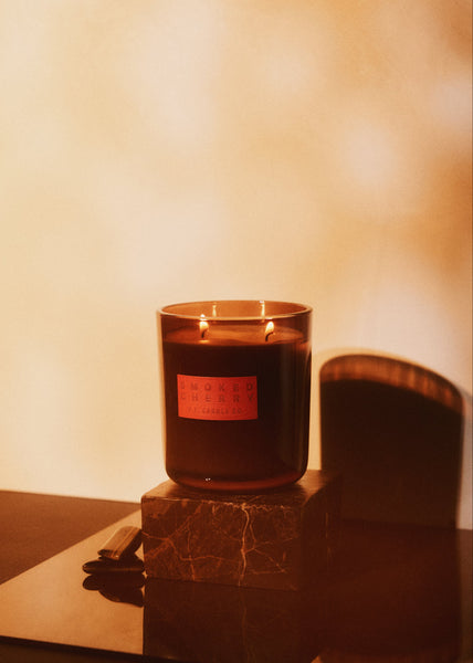 Candle in a glass holder with a red label on a marble surface.