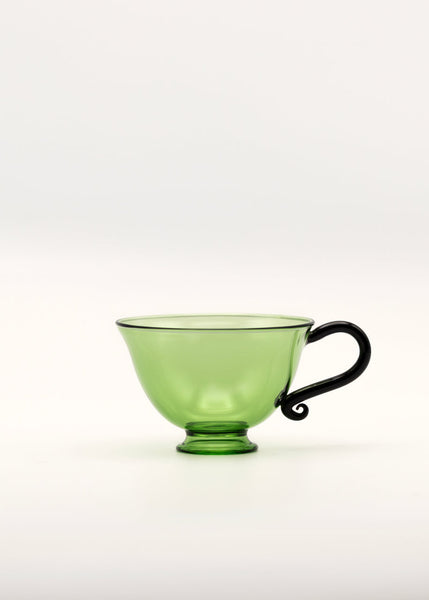 Green glass teacup with black handle on a white background