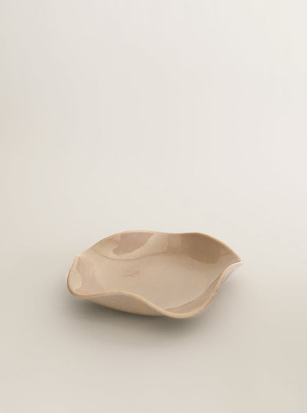 Sophie Lou Jacobsen's almond colored glass plate with a petal shaped wavy rim sits on a white background