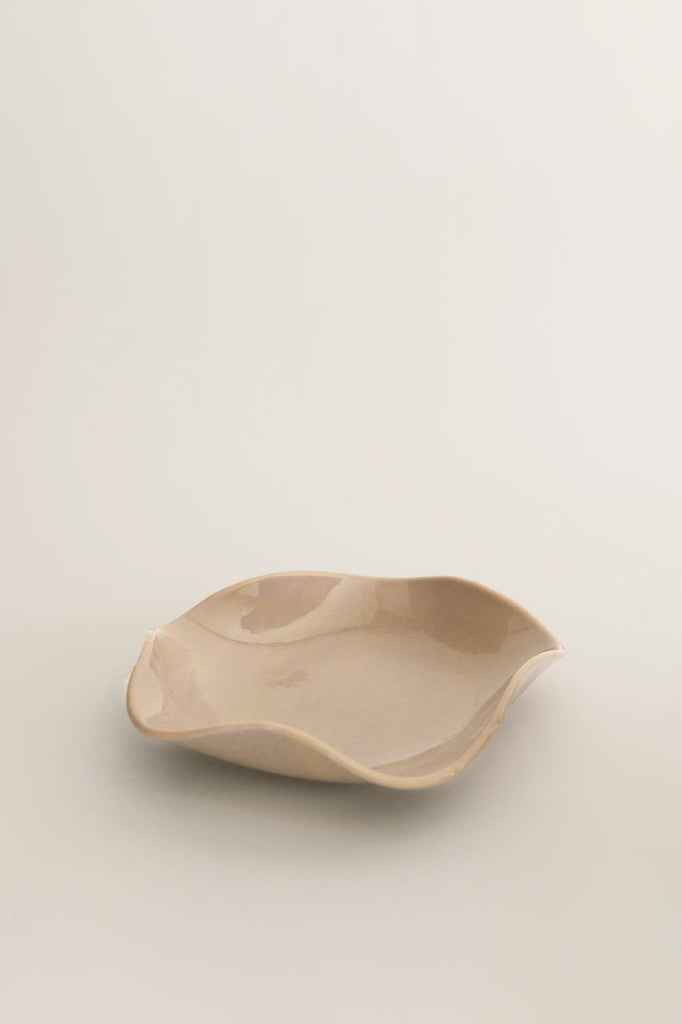 Sophie Lou Jacobsen's almond colored glass plate with a petal shaped wavy rim sits on a white background