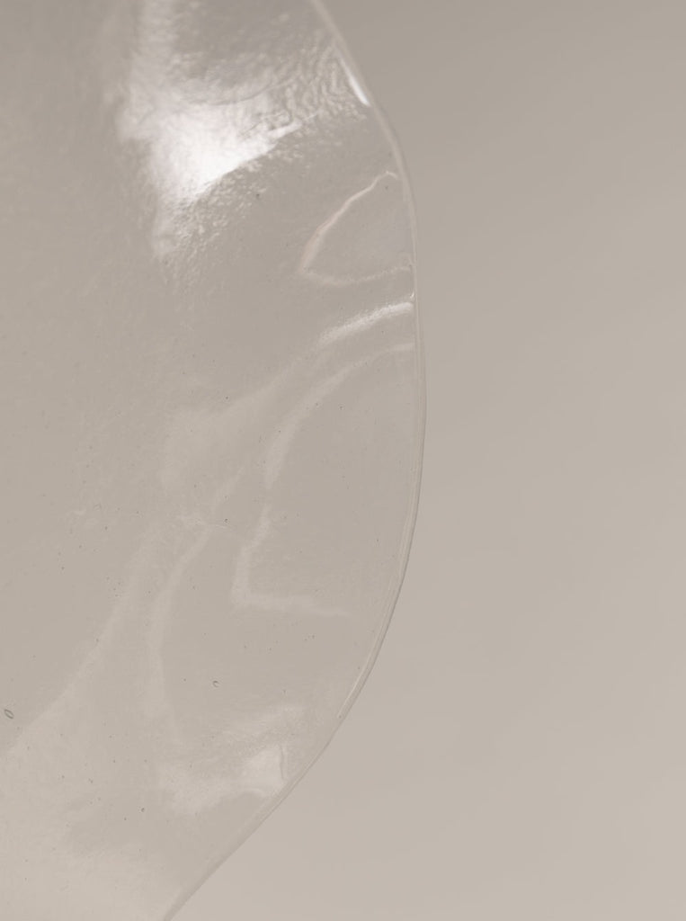 detail of Sophie Lou Jacobsen's opal clear colored glass plate with a petal shaped wavy rim sits on a white background