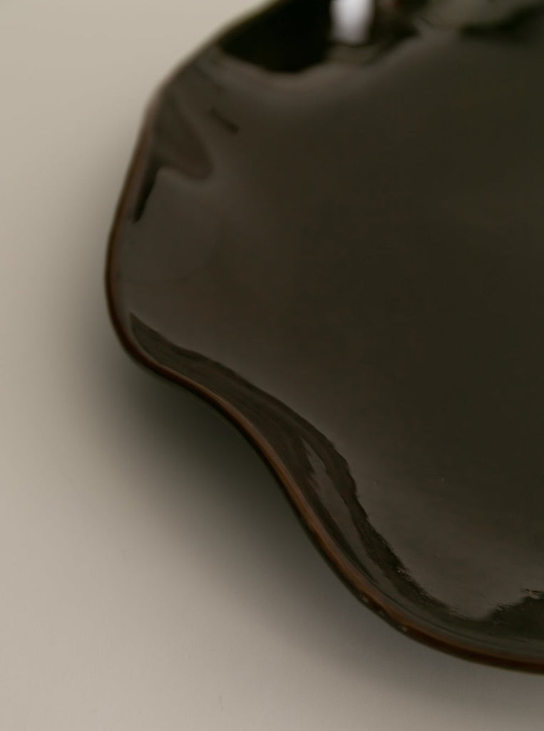 detail of Sophie Lou Jacobsen's pecan brown colored glass plate with a petal shaped wavy rim sits on a white background