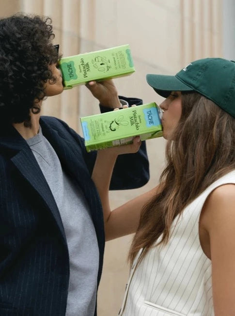 Two women drink from cartons of Táche barista blend pistachio milk cartons.