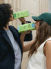 Two women drink from cartons of Táche barista blend pistachio milk cartons.