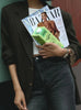 A women leans against a wall holding a stack of magazines and a carton of Táche Original Barista Blend Pistachio Milk